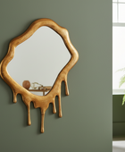 Wooden mirror with a unique design on a green wall next to a potted plant.