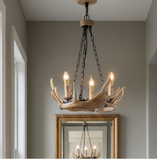 A rustic chandelier made from natural antlers with five candle-style bulbs, hanging in a hallway with a gold-framed mirror below.