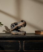 Dinosaur skull model, potted plant, and book on a wooden surface with a beige wall background