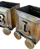 Two metal train car models with 'E' and 'L' on a wooden surface