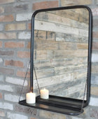 Decorative mirror with a shelf hanging against a brick wall.