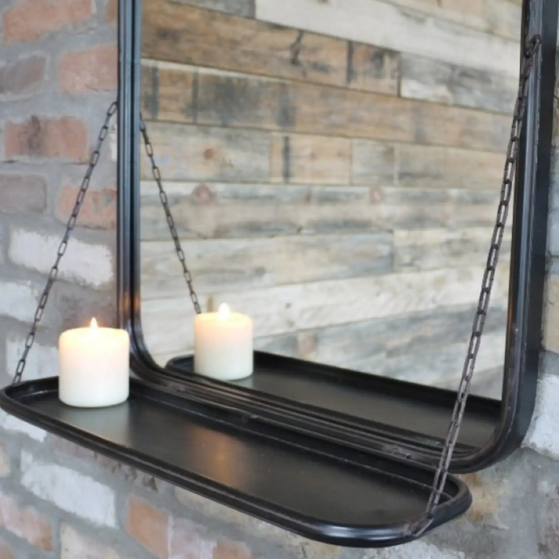 Black hanging mirror with a shelf against a brick wall.