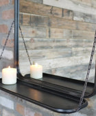 Black hanging mirror with a shelf against a brick wall.