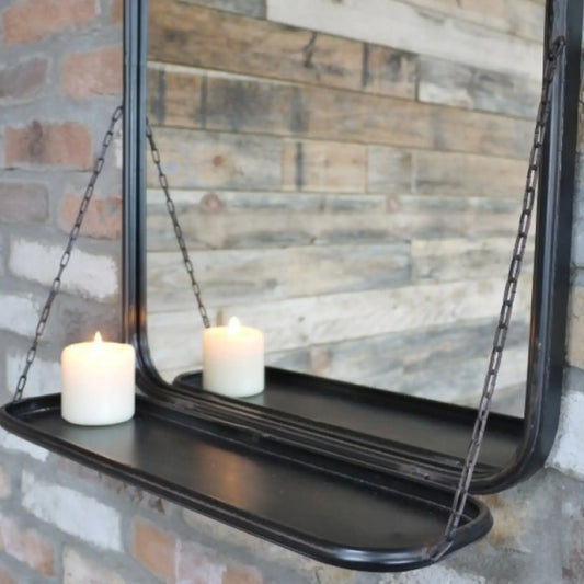 Black hanging mirror with a shelf against a brick wall.