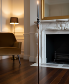 Tall candle on a stand in a room with a fireplace and chair.