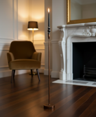 Tall floor lamp with a candle-like top in a room with a chair and fireplace.