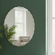 Decorative oval mirror on a green wall with a blurred indoor background