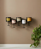 Wall-mounted candle holders with vintage-style labels against a beige wall, accompanied by a potted plant.
