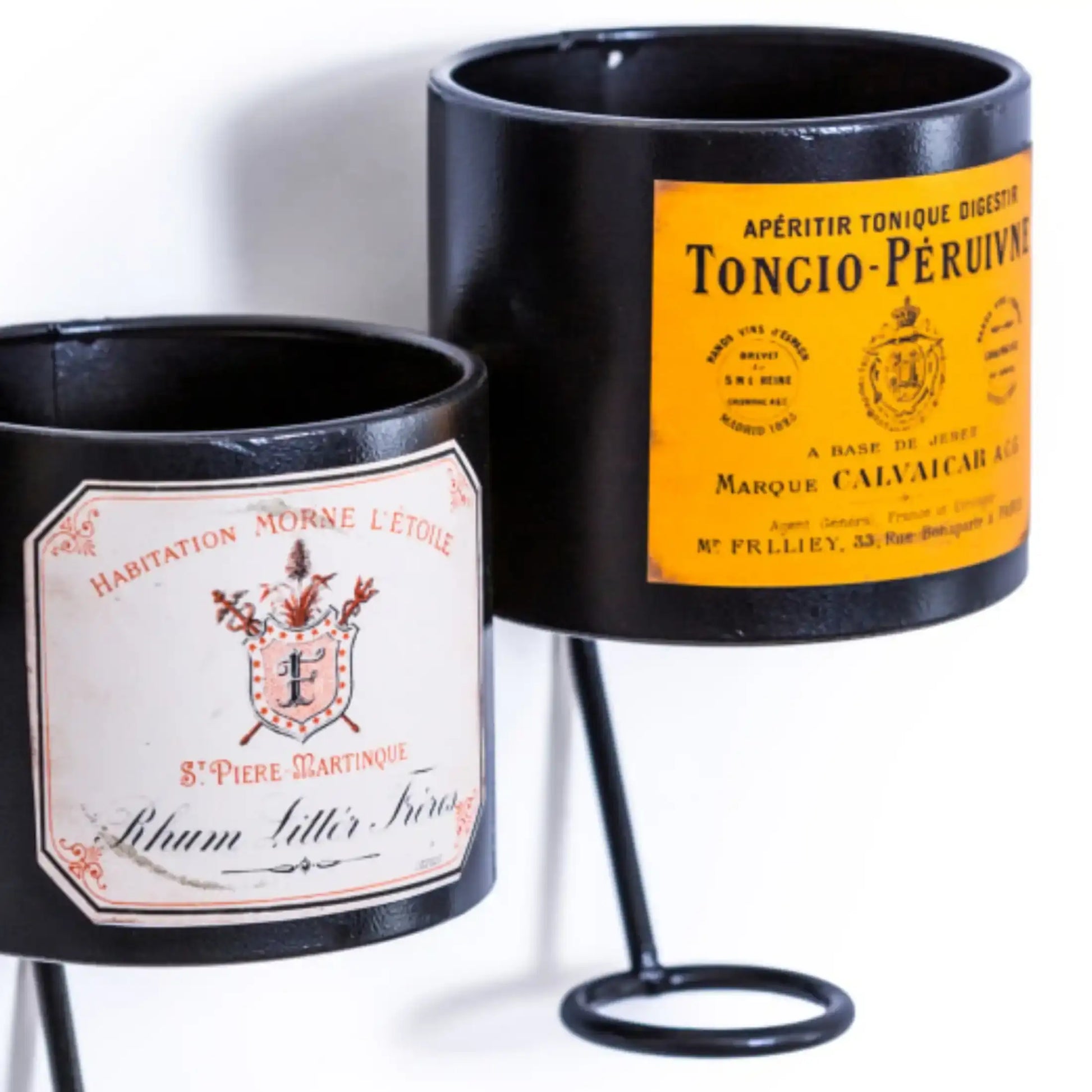 Two black candle holders with vintage-style labels on a white background