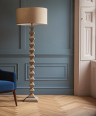 Tall floor lamp with a beige lampshade in a room with blue walls and wooden flooring.