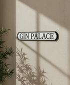 Decorative sign with 'Gin Palace' text on a beige wall with plant shadows.