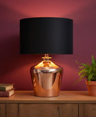 Table lamp with black shade and copper base on a wooden surface against a purple wall