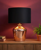 Table lamp with black shade and metallic base on a wooden surface against a purple wall.