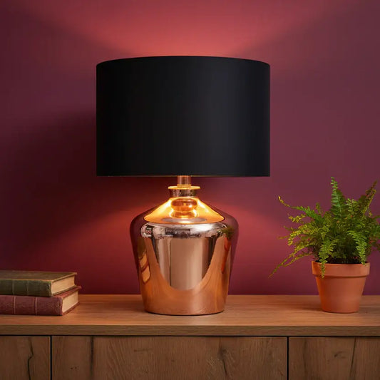 Table lamp with black shade and metallic base on a wooden surface against a purple wall.