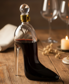 Bottle shaped like a high-heeled shoe filled with red liquid on a wooden table.