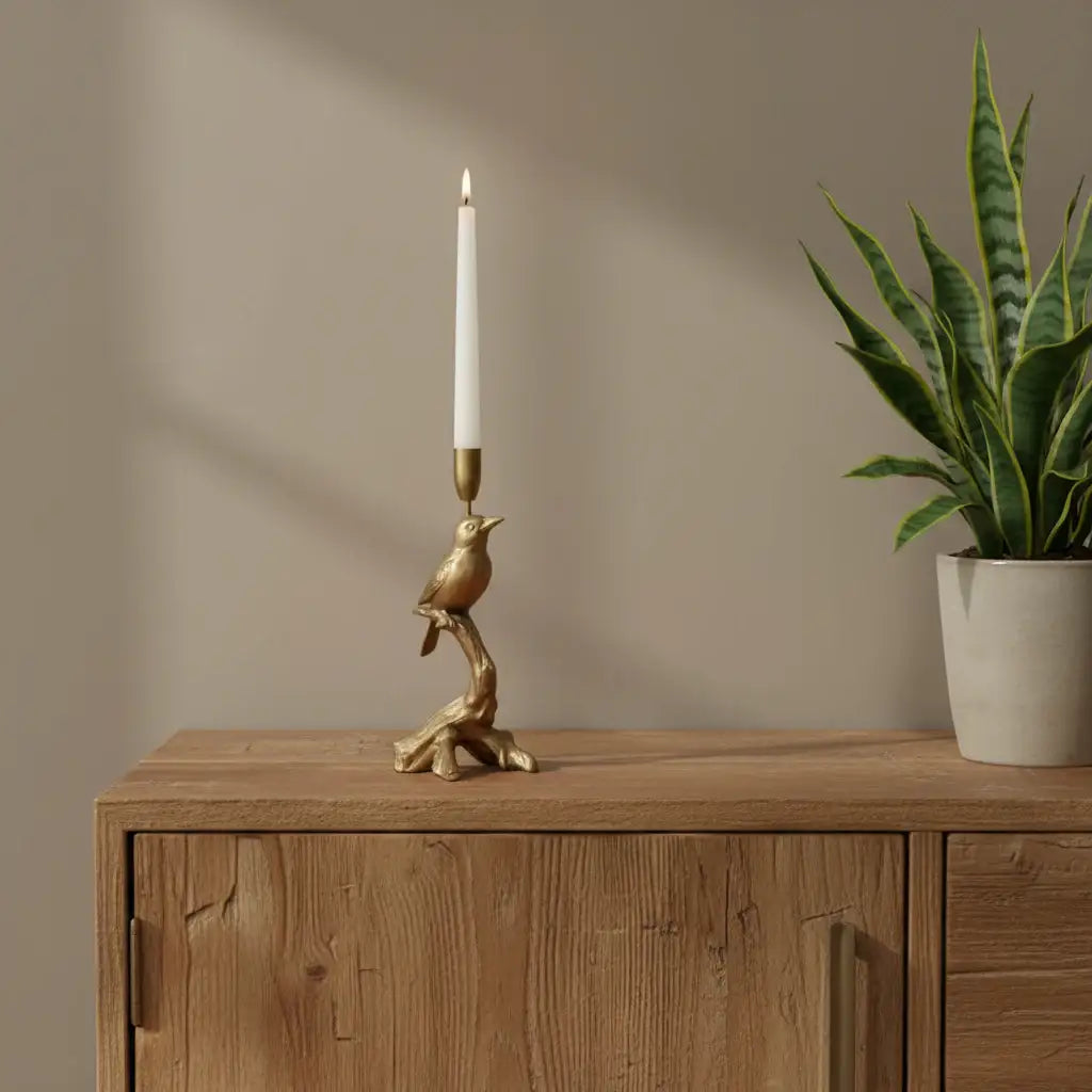 Decorative candle holder with bird design on a wooden surface with books and a plant.