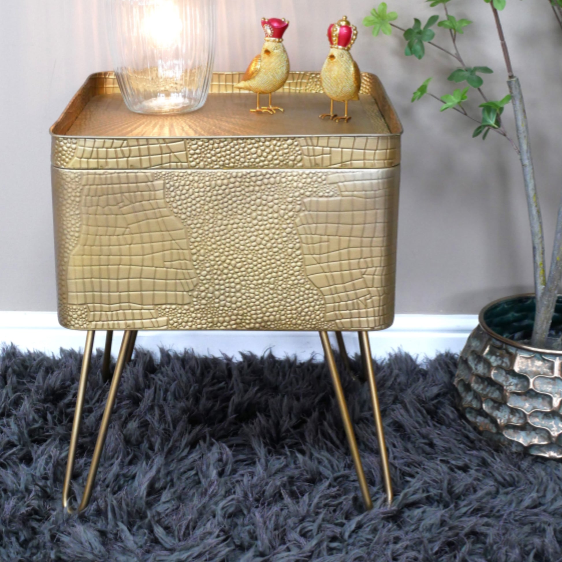 Gold textured side table with decorative items on a dark rug
