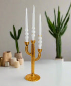 Gold cactus-shaped candle holder with white candles on a neutral background