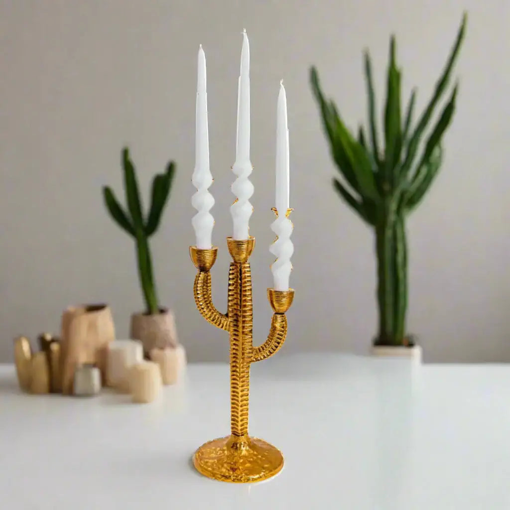 Gold cactus-shaped candle holder with white candles on a neutral background