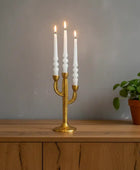 Gold candle holder with white candles on a wooden surface against a gray wall.