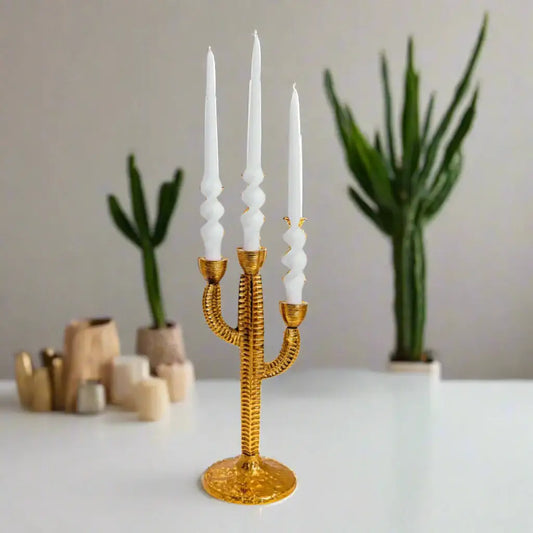 Gold cactus-shaped candle holder with white candles on a neutral background