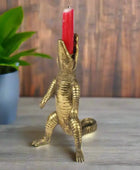 Gold alligator candle holder with a red candle on a wooden surface with a plant in the background