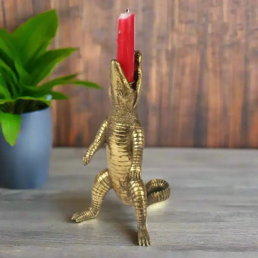 Gold alligator candle holder with a red candle on a wooden surface with a plant in the background