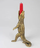 Brass alligator candle holder with a red candle on a white background