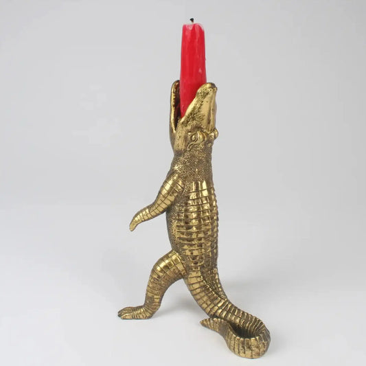 Brass alligator candle holder with a red candle on a white background