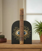 Decorative bookend with eye design on a wooden surface with books and a plant in the background.