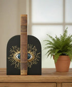 Decorative bookends with eye design on a wooden surface next to a potted plant.