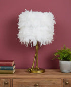 Feathered lamp on a wooden sideboard with books and a plant against a pink wall