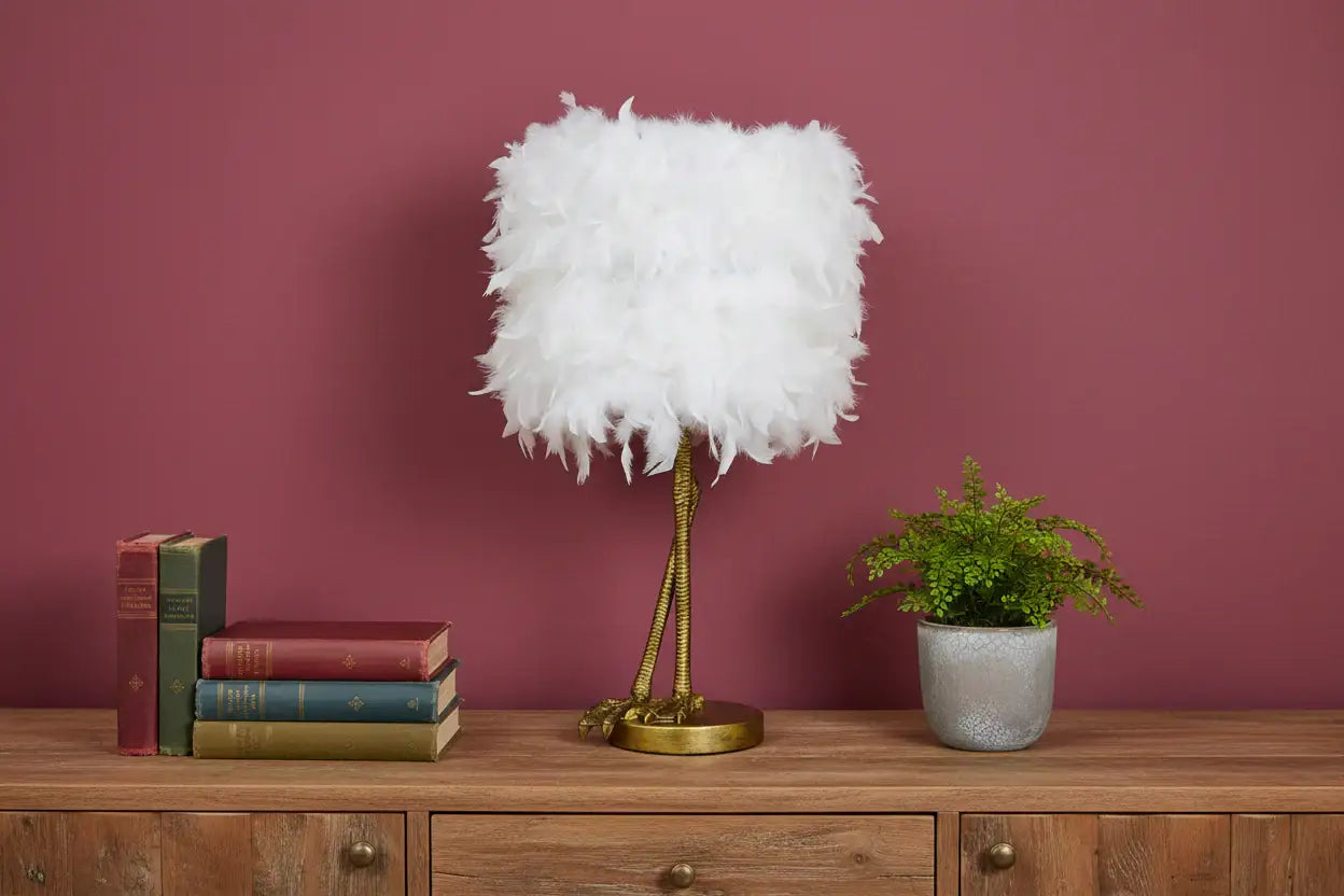 Feathered lamp on a wooden sideboard with books and a plant against a pink wall