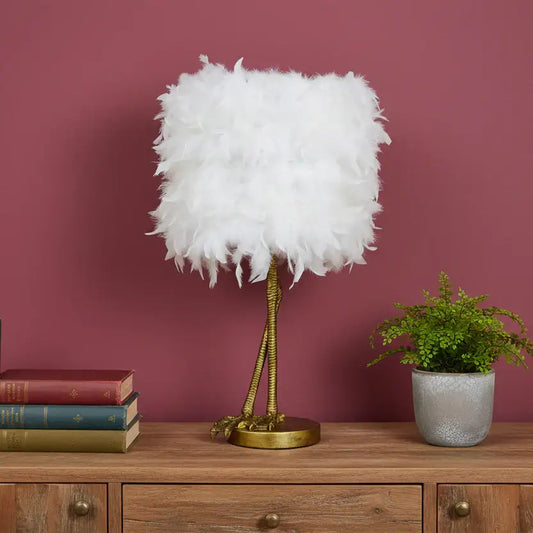 Feathered lamp on a wooden dresser with books and a plant against a pink wall