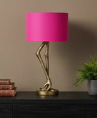 Table lamp with pink shade and gold base on a dark surface against a brown wall