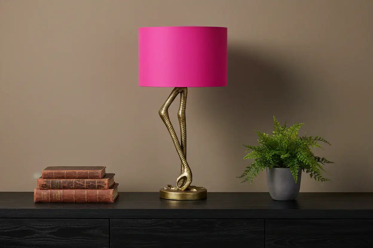 Table lamp with pink shade and gold base on a dark surface against a brown wall