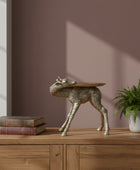 Gold deer-shaped side table on a wooden surface with a brick wall background