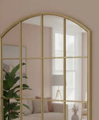 Gold-framed arch mirror on a beige wall with a blurred room background