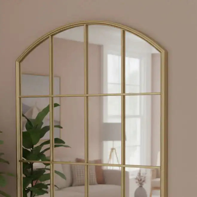 Gold-framed arch mirror on a beige wall with a blurred room background
