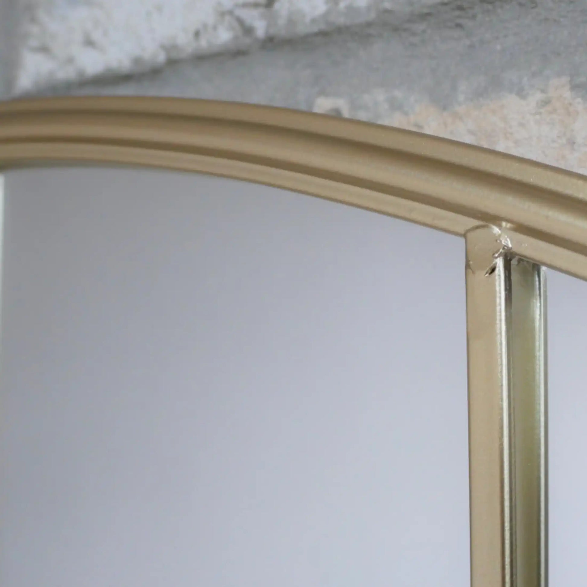 Gold-framed mirror on a white wall with a textured gray background