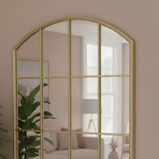 Gold-framed arch mirror on a beige wall with a blurred room background