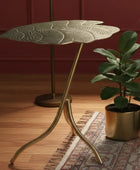 Decorative side table with leaf design against a teal wall.