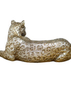 Gold leopard figurine on a wooden surface with a stone wall background