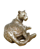 Bronze panther figurine on a wooden surface with a stone wall background
