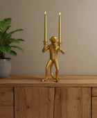 Gold monkey candle holder with two lit candles on a wooden surface next to a plant.
