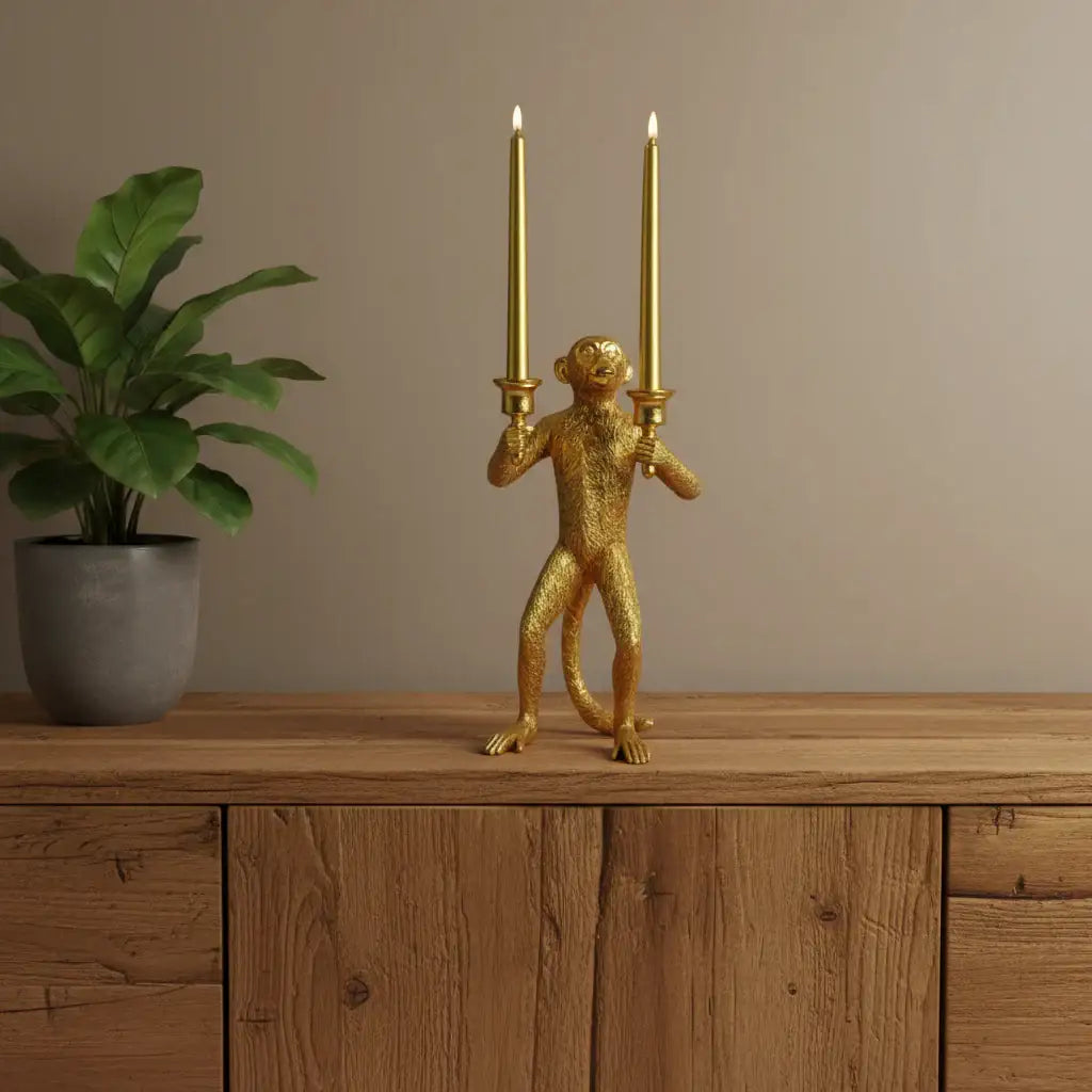 Gold monkey candle holder with two lit candles on a wooden surface next to a plant.