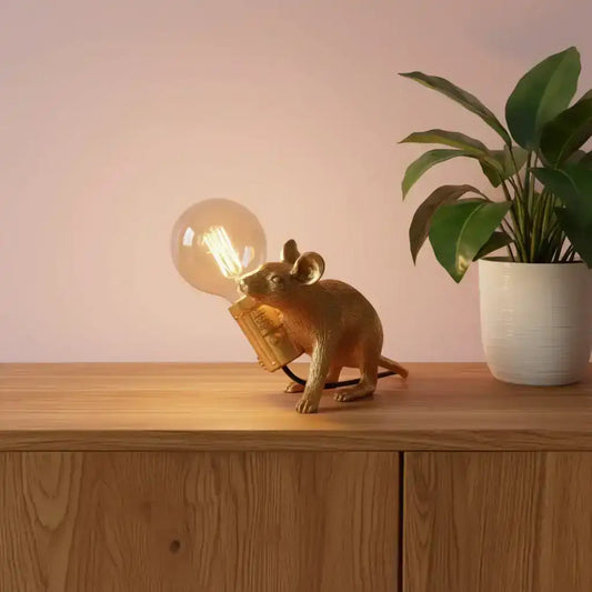 Gold mouse figurine with a lit light bulb on a surface, with a blurred background.