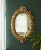 Decorative gold mirror on a green wall with a plant in the corner