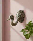 Bronze flamingo wall hook on a pink wall with a plant in the corner