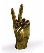 A metallic gold sculpture of a hand making the peace sign, set against a plain white background.